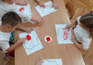 Dzieci malują palcami przy stolikach