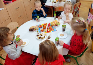 Dzieci siedzą przy stolikach i częstują się słodyczami