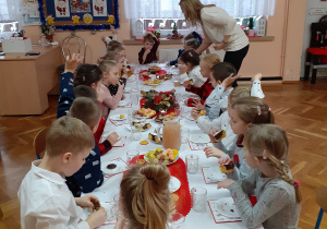 Dzieci siedzą i częstują się owocami i słodyczami
