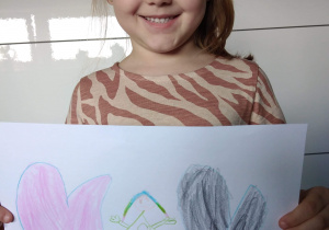 Lenka z uśmiechem pokazuje swój rysunek.