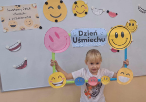 Hania trzyma w rękach ramkę z emotkami uśmiechu.