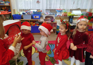 Dzieci przykleją czerwone karteczki do czapki Mikołaja.