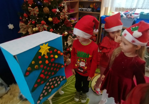 Dzieci naklejają kolorowe pompony do choinki.