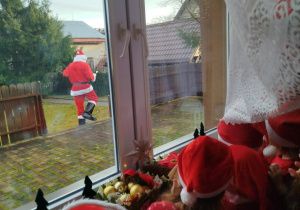 Dzieci wyglądają przez okno i obserwują Mikołaja.