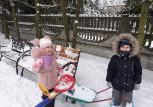 Dziewczynki wiozą śnieg na taczce.