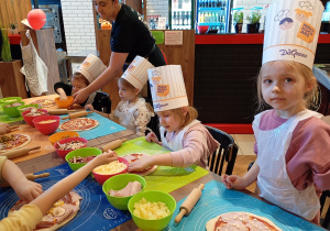 Dzieci przy stole wykonija swoją pizzę.