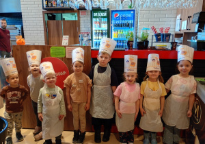 Dieci ubrane w fartuszki i czapki czekją na pizzę poskończonej pracy.