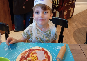 Chłopiec doodaje składniki do swojej pizzy.