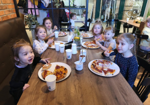 Dzieci jedzą pizzę.